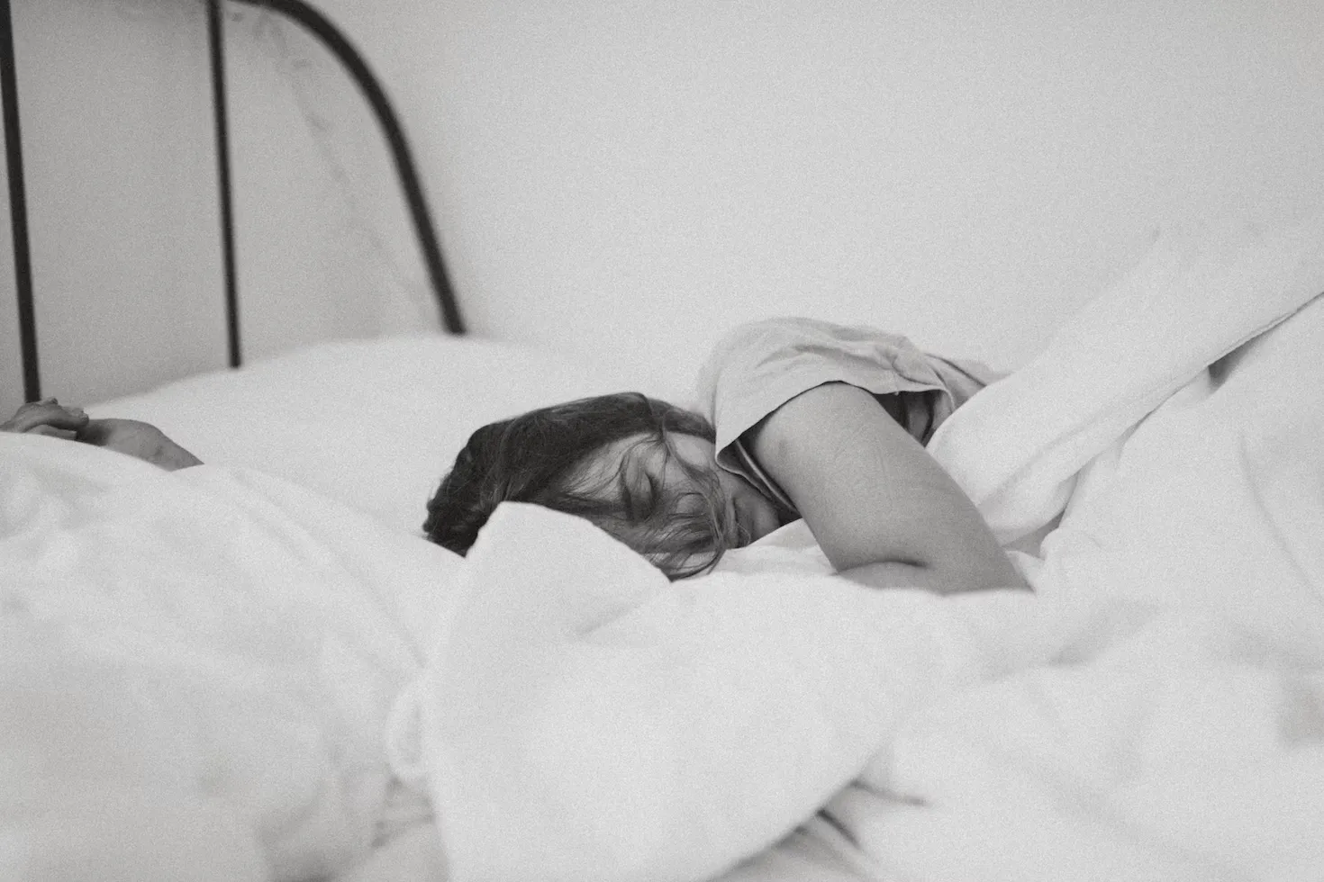 

A woman lying in bed, surrounded by plants and natural light, peacefully sleeping.